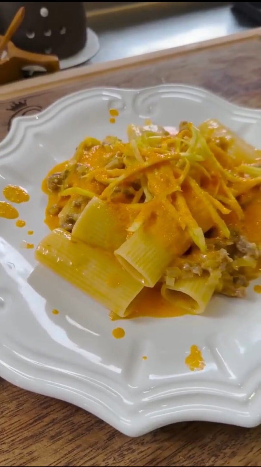 A white plate with rigatoni pasta topped with a rich orange sauce and shredded cheese, garnished with small pieces of meat.