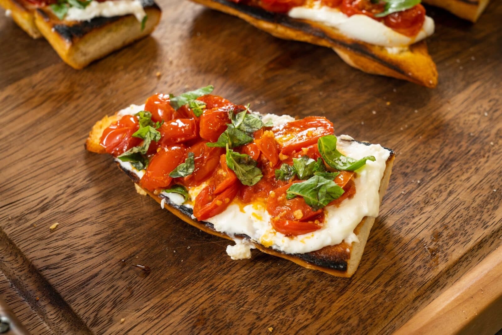 Toasted bread topped with melted cheese, roasted tomatoes, and fresh basil on a wooden surface.