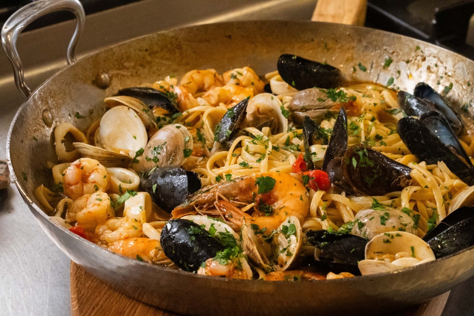 A pan of seafood pasta with shrimp, clams, mussels, and linguine, garnished with chopped parsley.