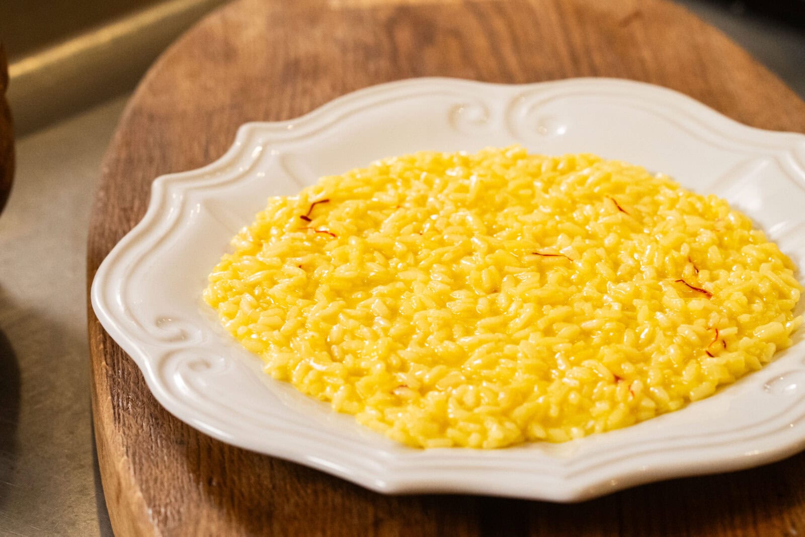 A plate of yellow saffron risotto is served on a white ornate dish placed on a wooden surface.