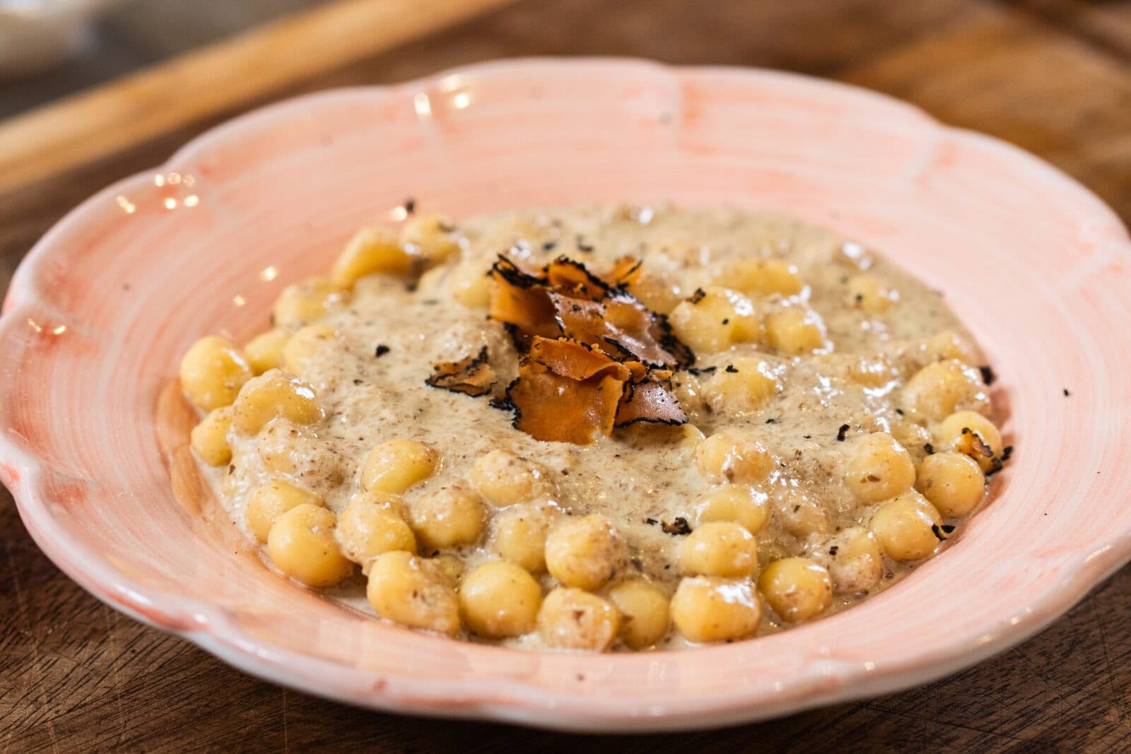 A plate of gnocchi in a creamy sauce, topped with shaved black truffle, served on a pink ceramic dish.