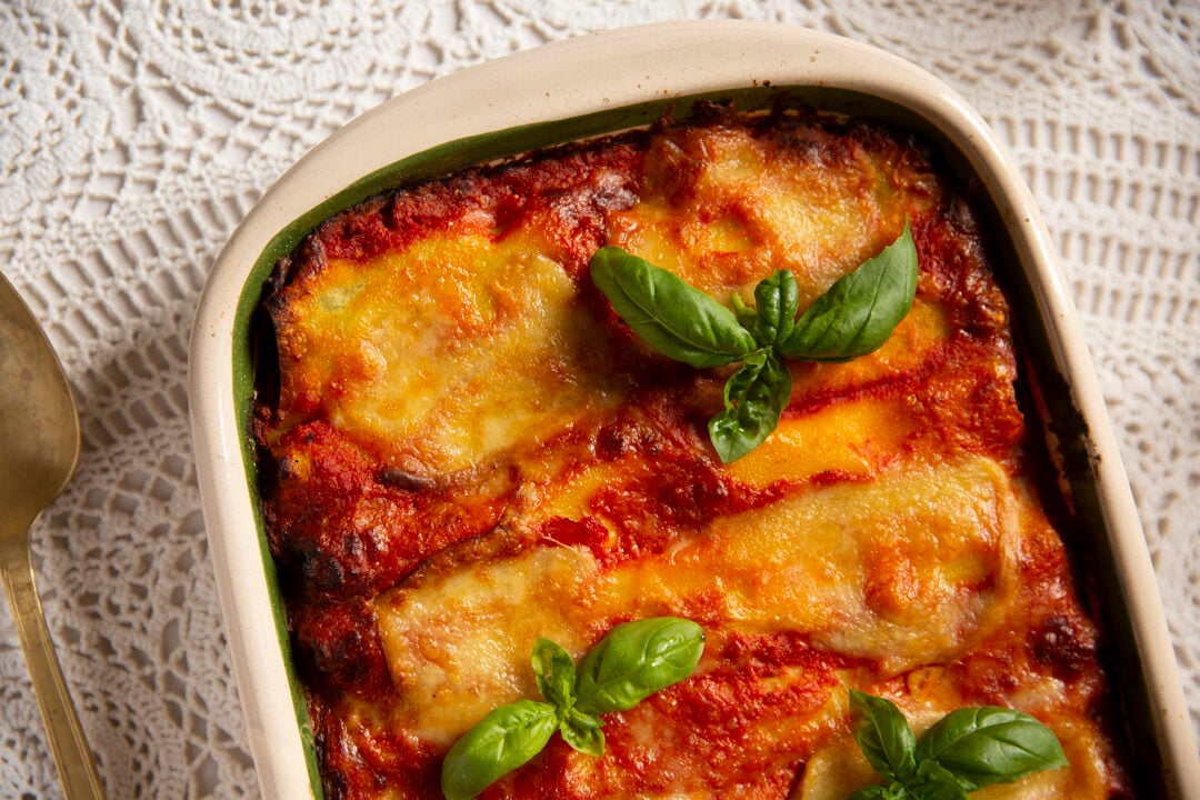 A baked dish of lasagna topped with melted cheese and garnished with fresh basil leaves, placed on a white lace tablecloth.