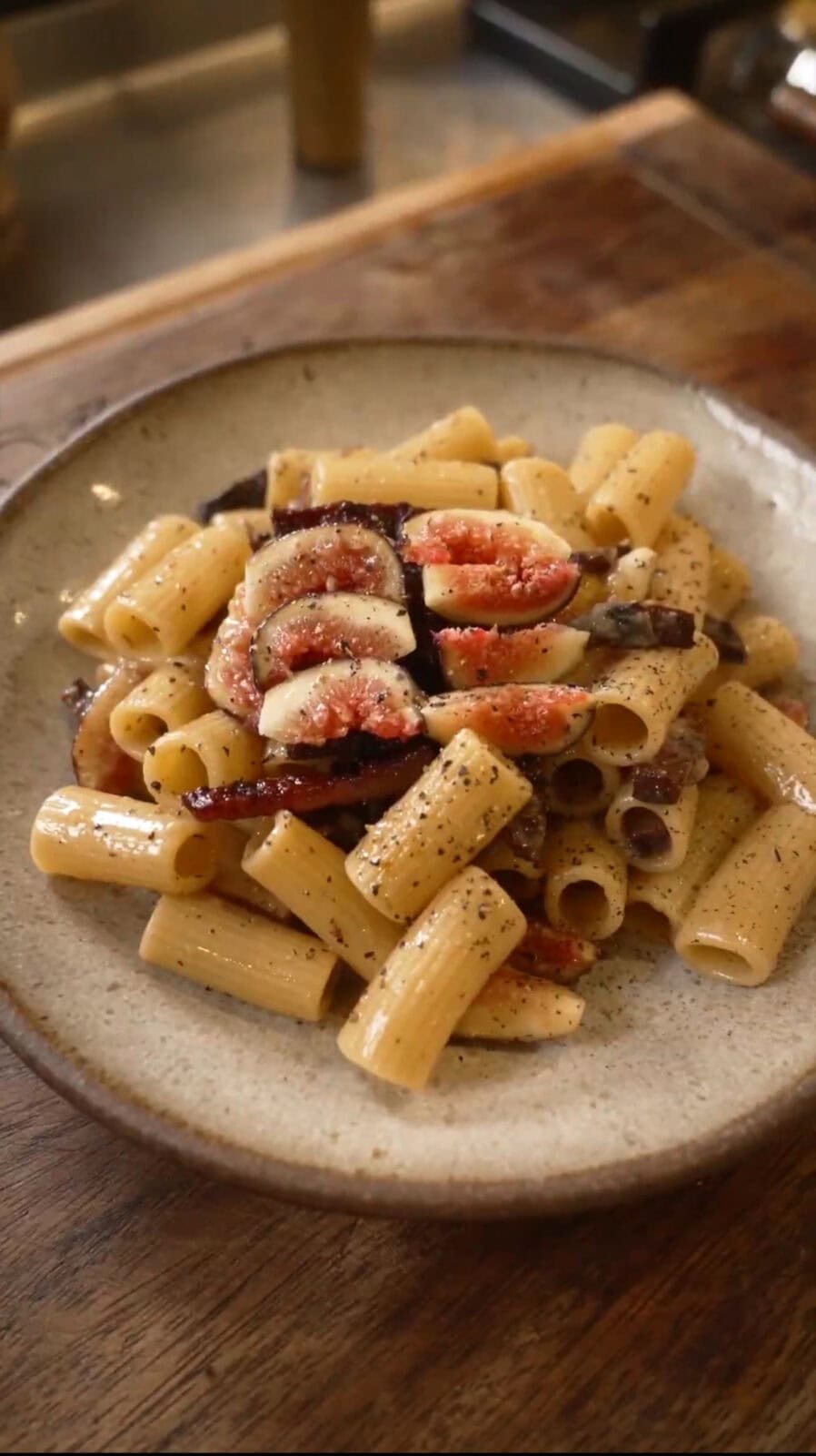 A plate of rigatoni pasta topped with sliced figs and red onion, seasoned with black pepper.
