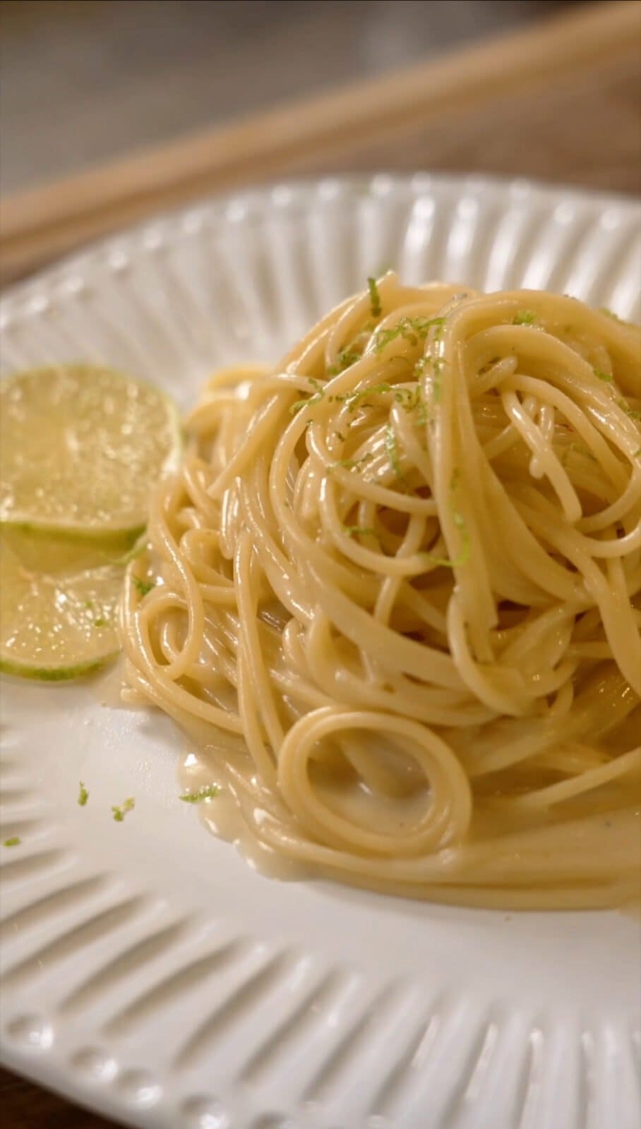 A plate of spaghetti noodles topped with grated lime zest, accompanied by two lime slices on the side.