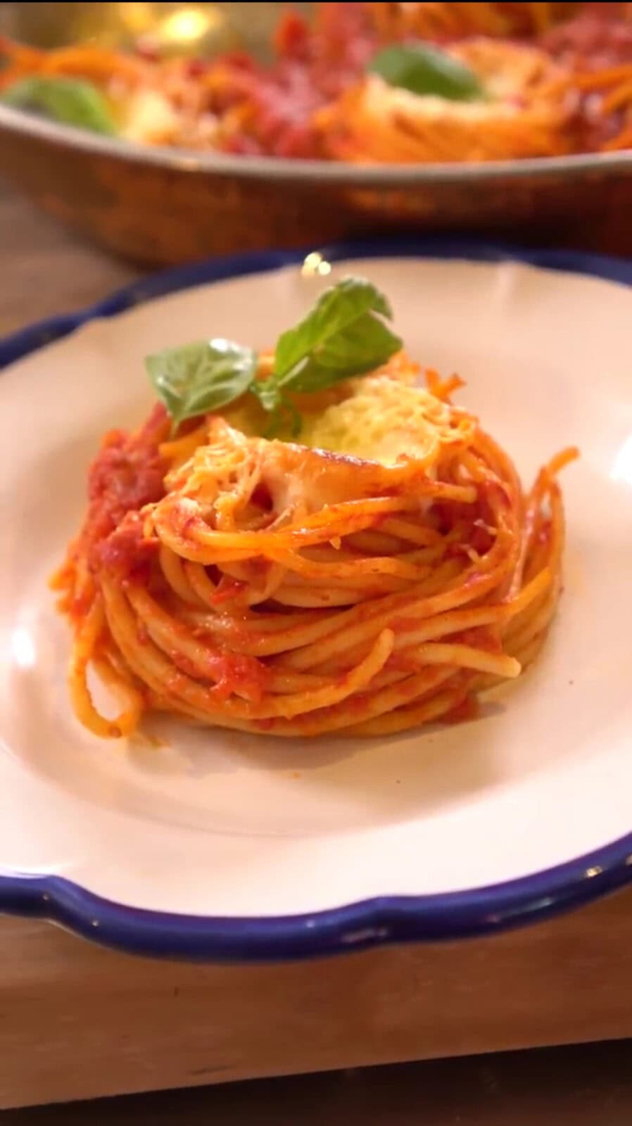 A plate of spaghetti with tomato sauce, garnished with basil leaves and a slice of cheese, served on a white dish with a blue rim.