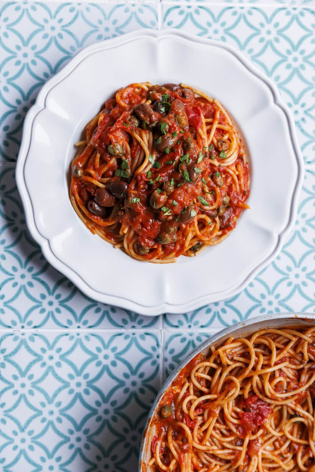 Plate of spaghetti with tomato sauce and herbs on a patterned blue and white tile surface.