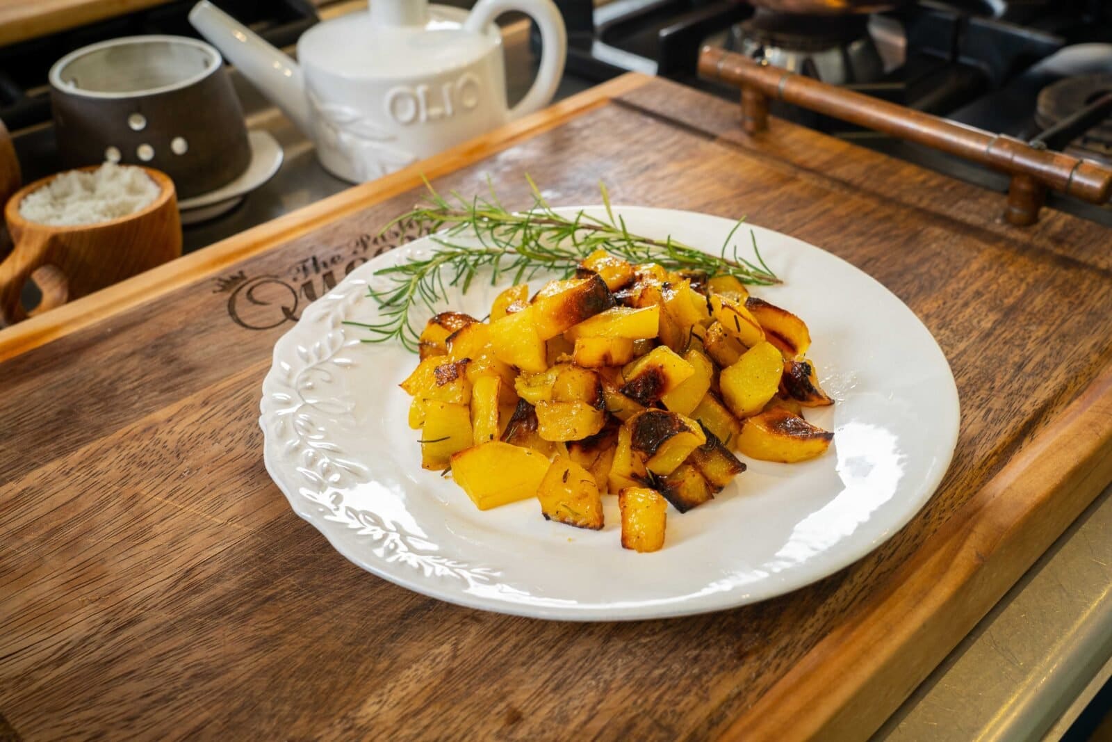 A plate of roasted yellow squash and zucchini garnished with rosemary on a wooden board in a kitchen setting.