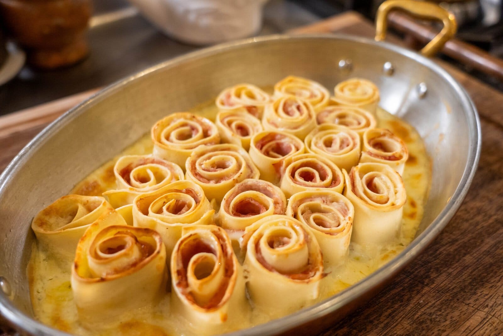 Baked pasta rolls with visible filling arranged in a circular pattern in a metal dish with a handle.