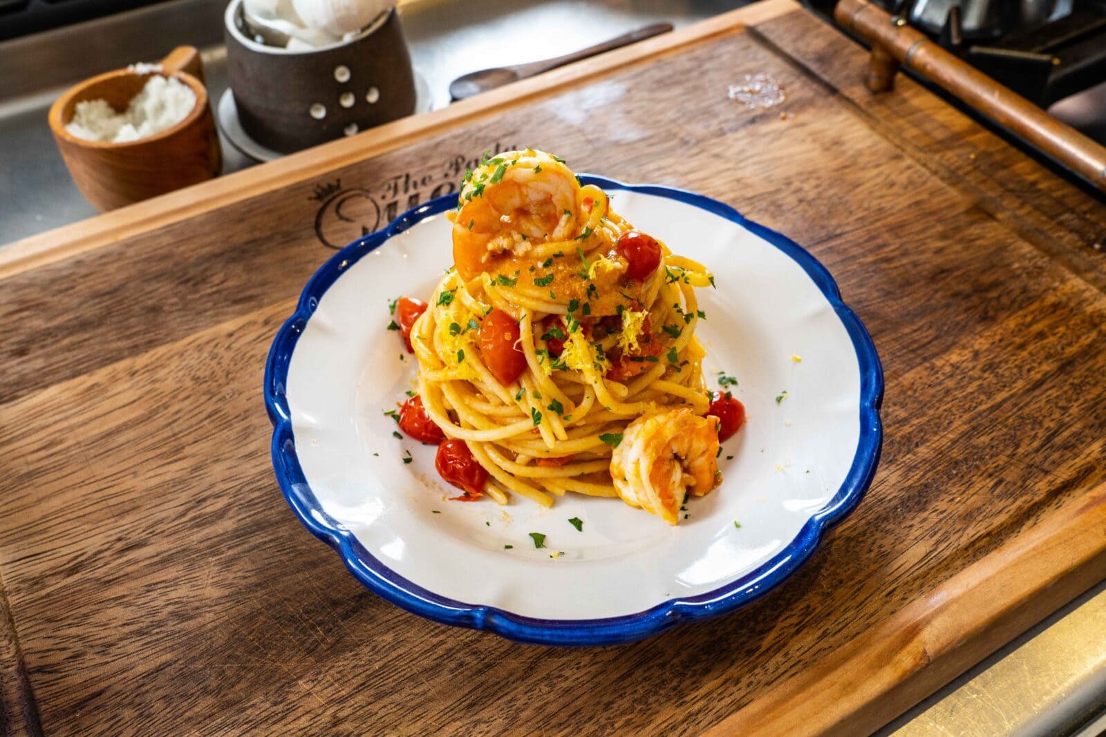 Plate of spaghetti topped with shrimp, cherry tomatoes, and parsley on a wooden board.