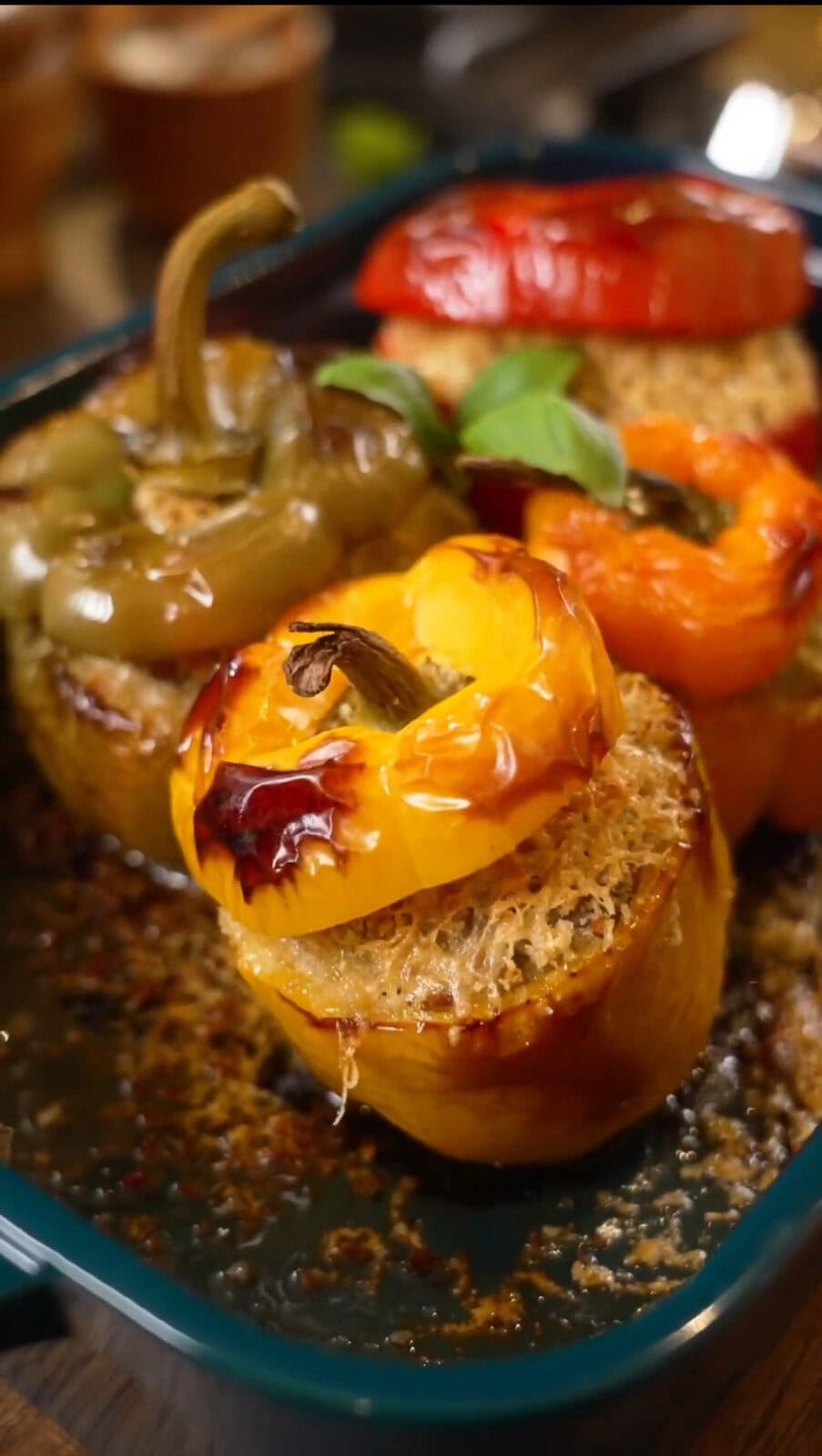 Three stuffed bell peppers (yellow, green, red) in a baking dish, filled with quinoa and topped with their respective caps.