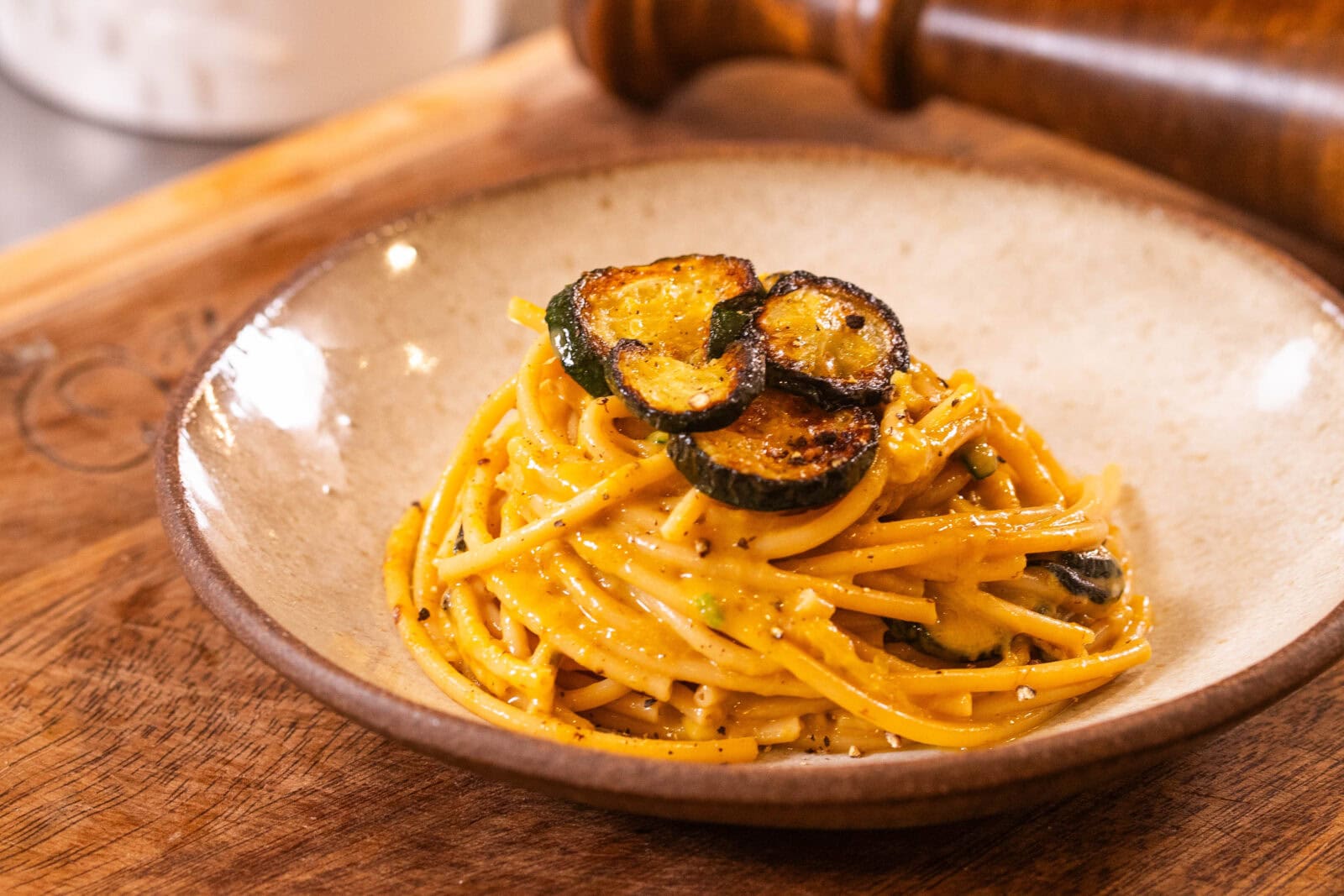 A plate of spaghetti in a creamy sauce topped with grilled zucchini slices, served on a wooden board.