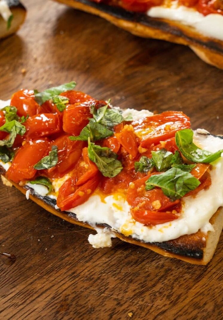 Toasted bread topped with melted cheese, roasted tomatoes, and fresh basil on a wooden surface.