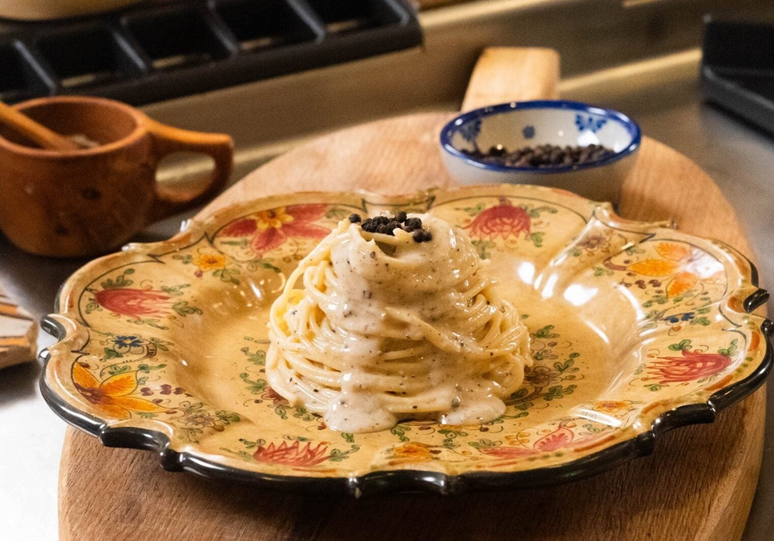A plate of spaghetti with creamy white sauce and ground black pepper is served on a decorative plate, with a small bowl of pepper in the background.