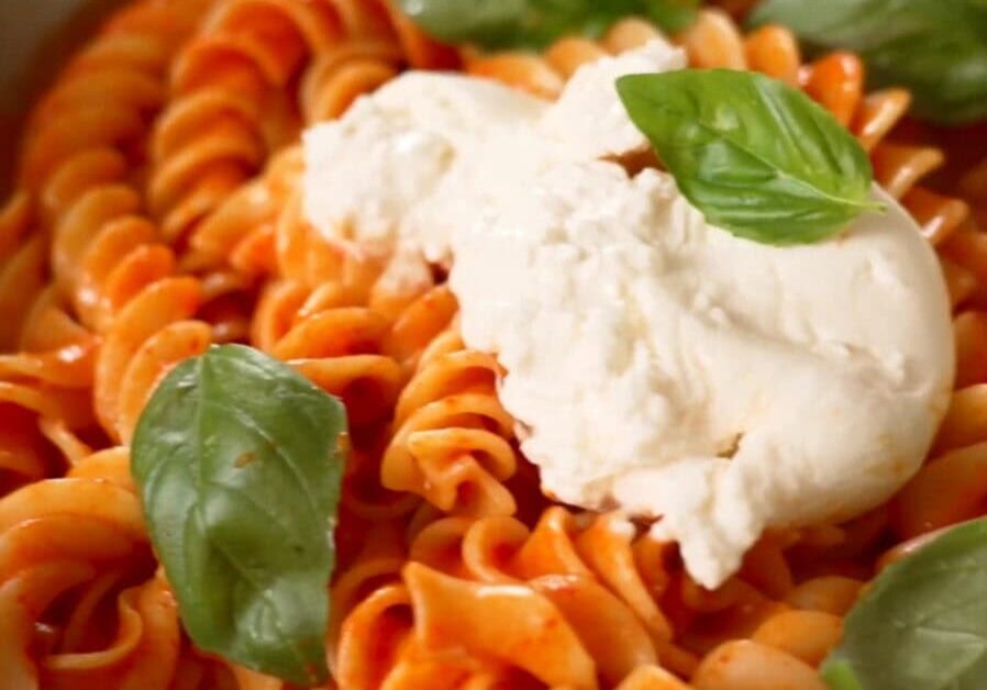 A plate of fusilli pasta with red sauce, topped with a dollop of ricotta cheese and garnished with fresh basil leaves.