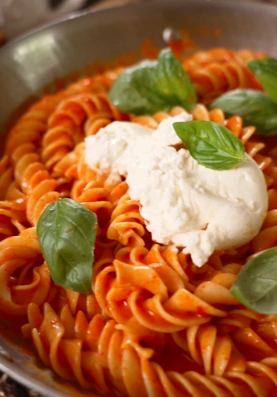 A plate of fusilli pasta with red sauce, topped with a dollop of ricotta cheese and garnished with fresh basil leaves.