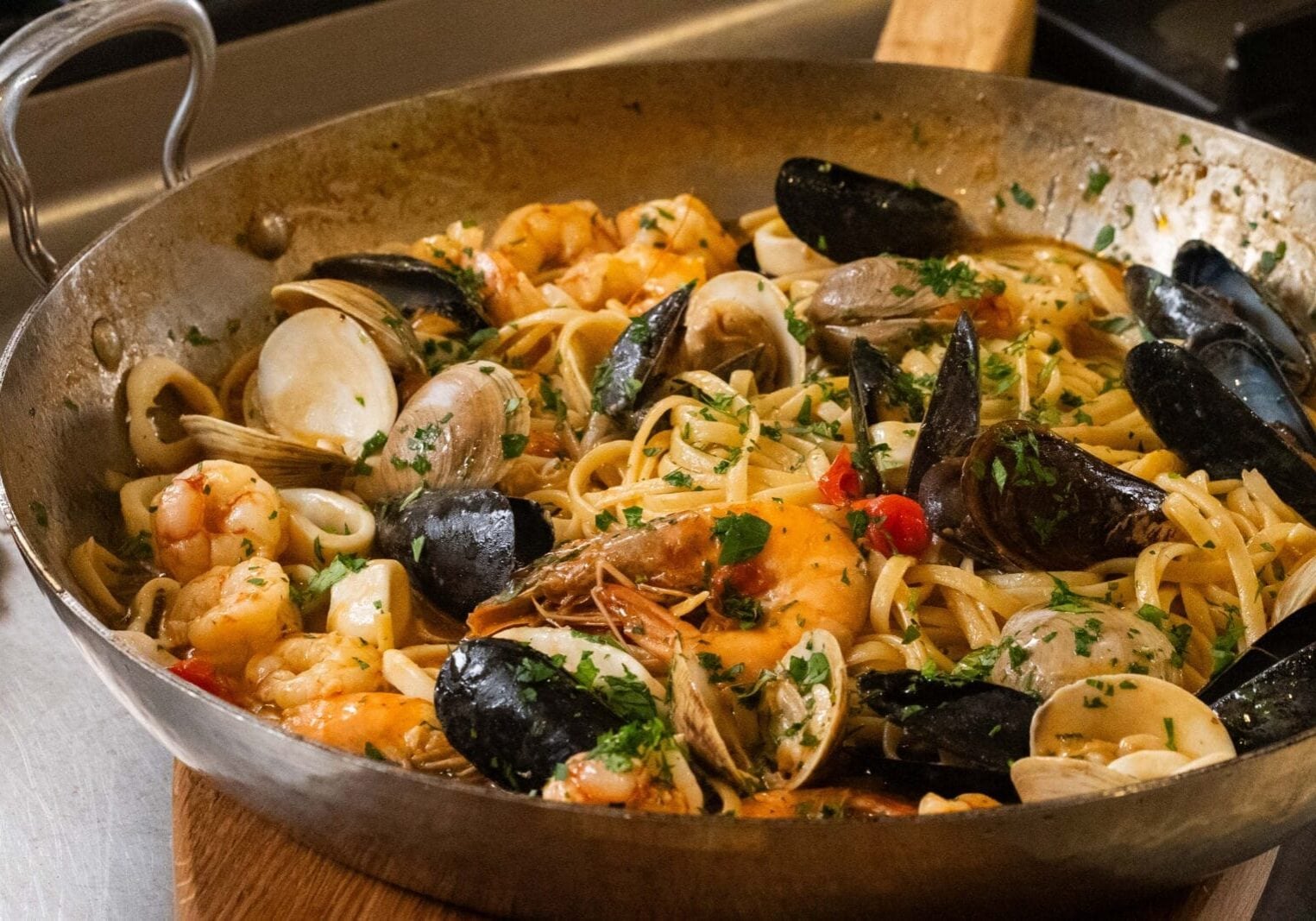 A pan of seafood pasta with shrimp, clams, mussels, and linguine, garnished with chopped parsley.