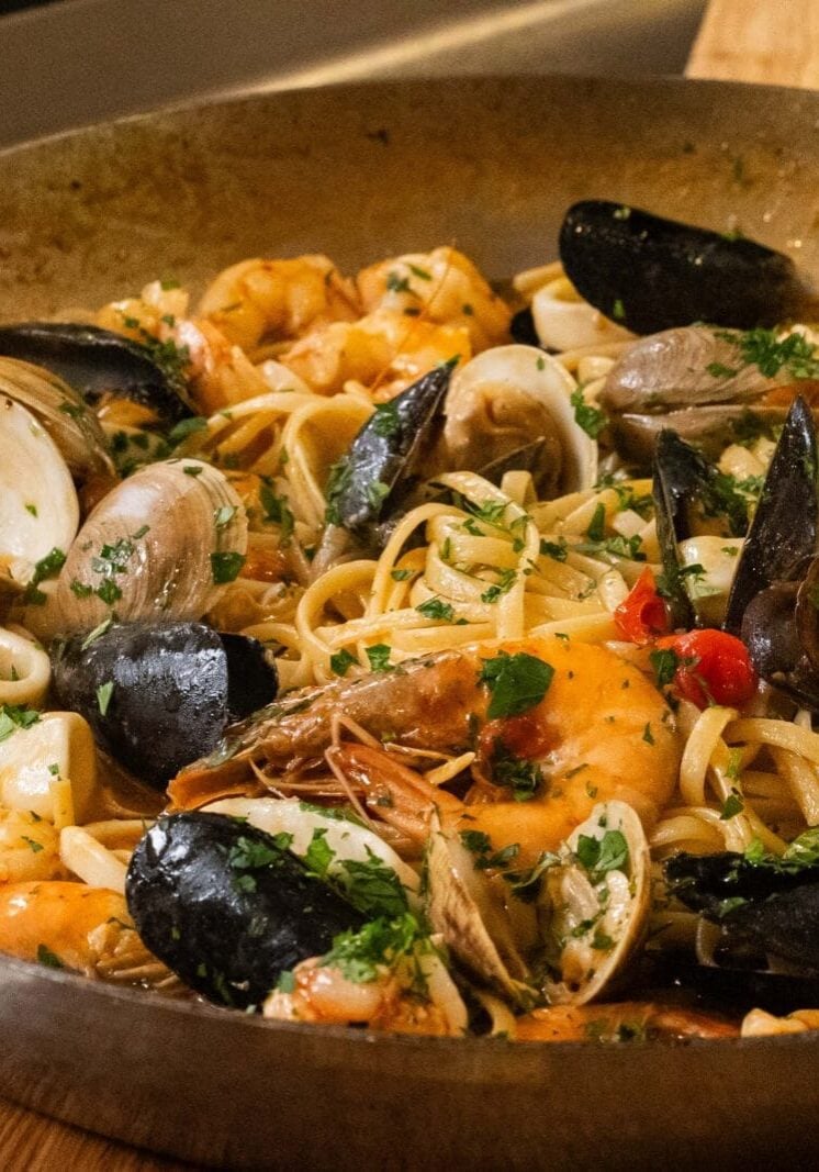 A pan of seafood pasta with shrimp, clams, mussels, and linguine, garnished with chopped parsley.
