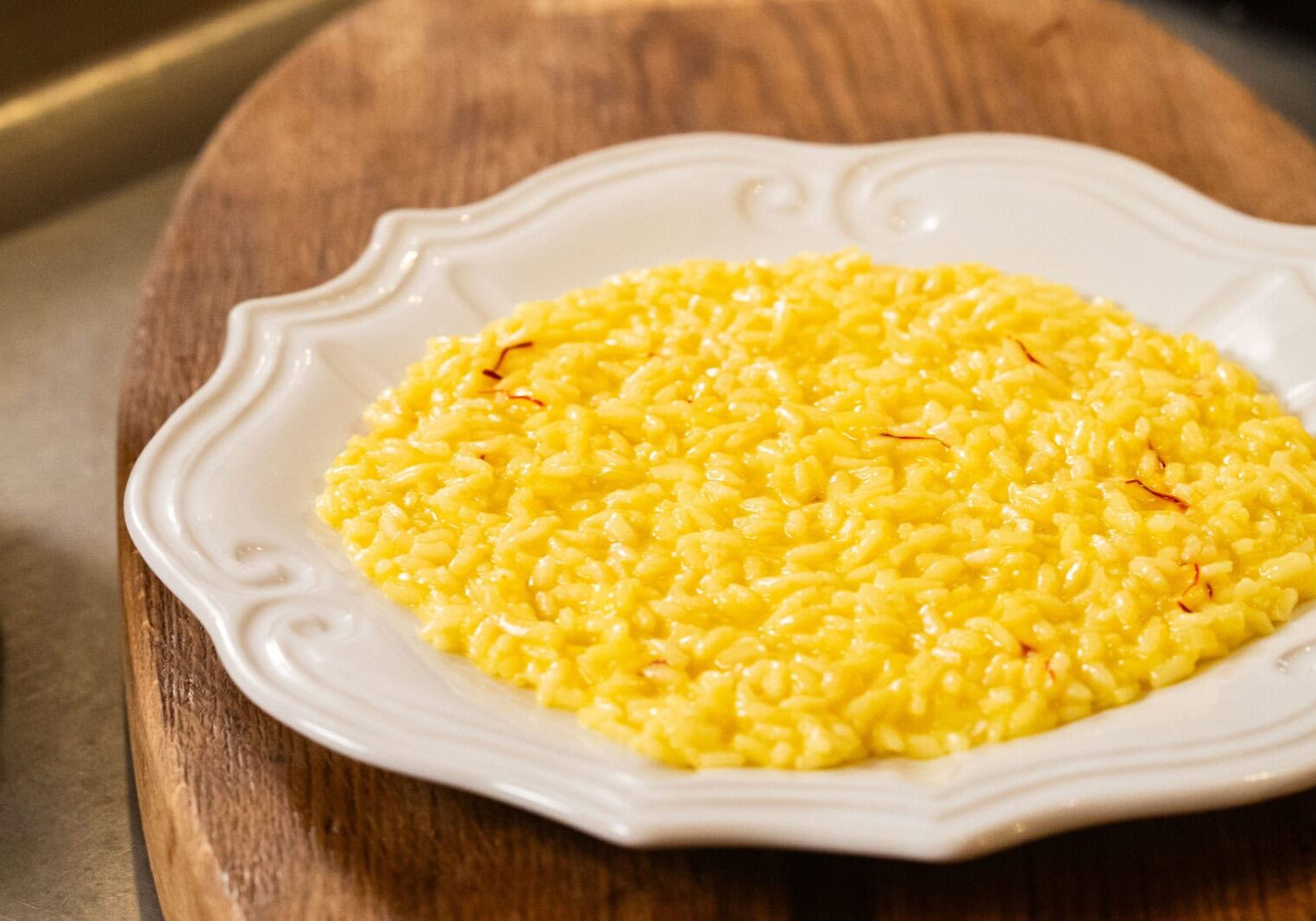 A plate of yellow saffron risotto is served on a white ornate dish placed on a wooden surface.