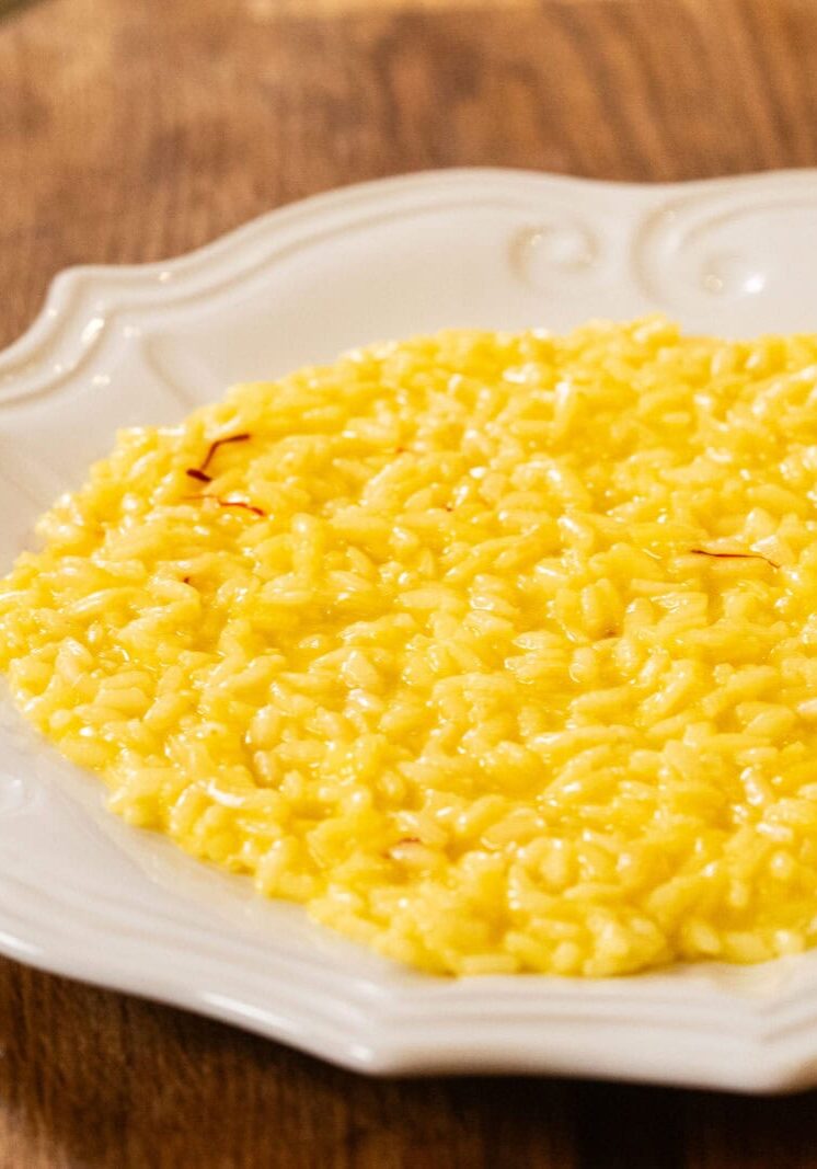 A plate of yellow saffron risotto is served on a white ornate dish placed on a wooden surface.