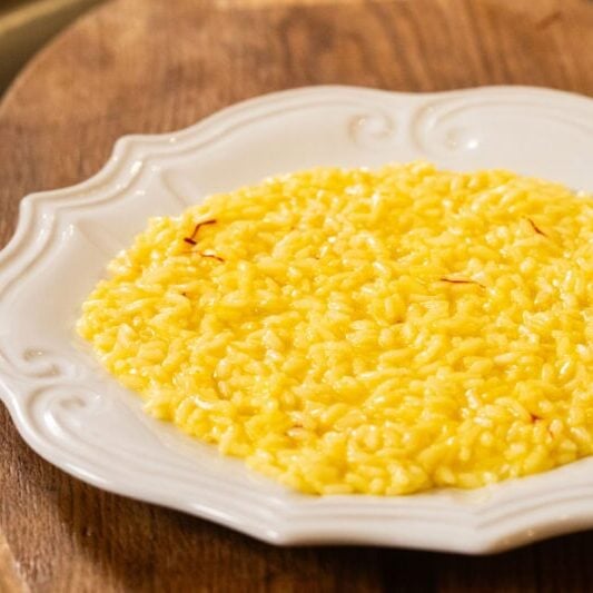 A plate of yellow saffron risotto is served on a white ornate dish placed on a wooden surface.