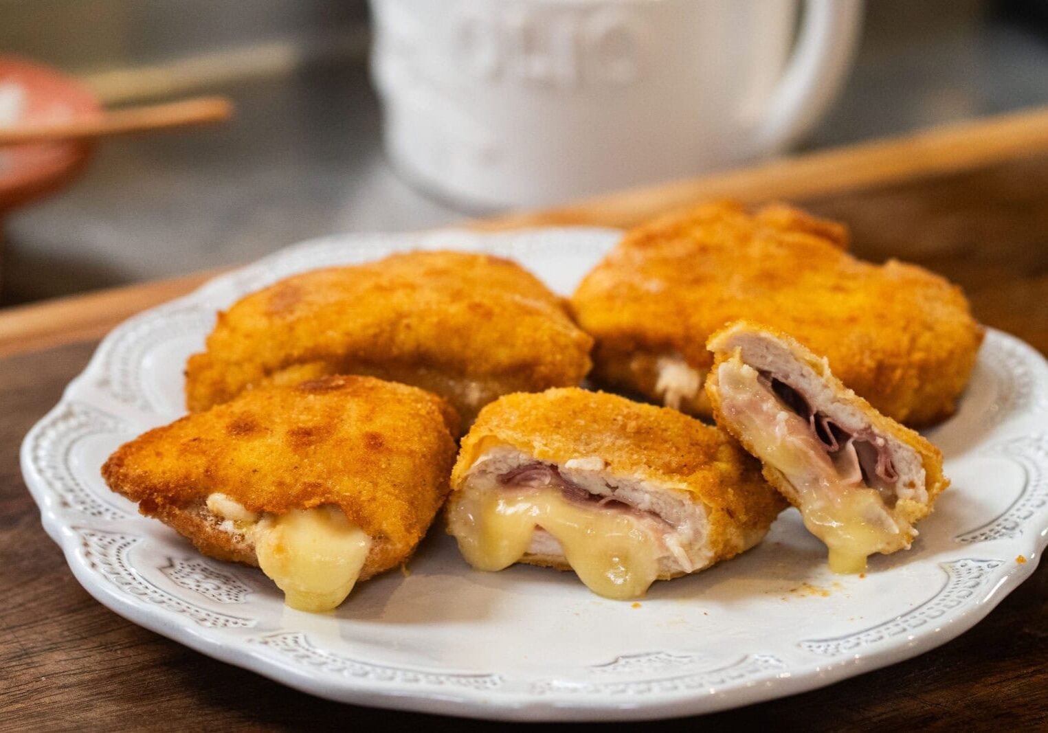Breaded and fried cutlets, some cut open to show melted cheese and ham filling, arranged on a white plate.
