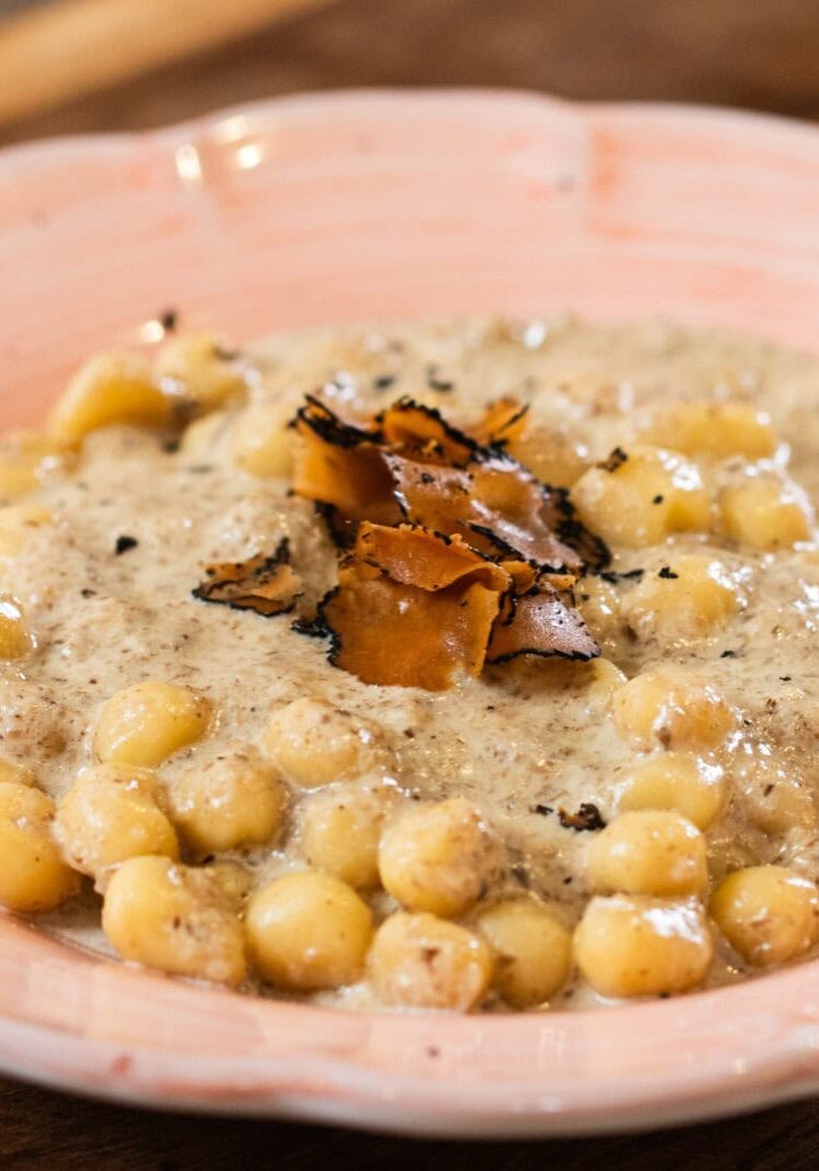 A plate of gnocchi in a creamy sauce, topped with shaved black truffle, served on a pink ceramic dish.