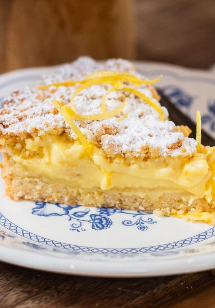 A slice of lemon cream pie with powdered sugar and lemon zest on top, served on a blue and white plate with a fork.