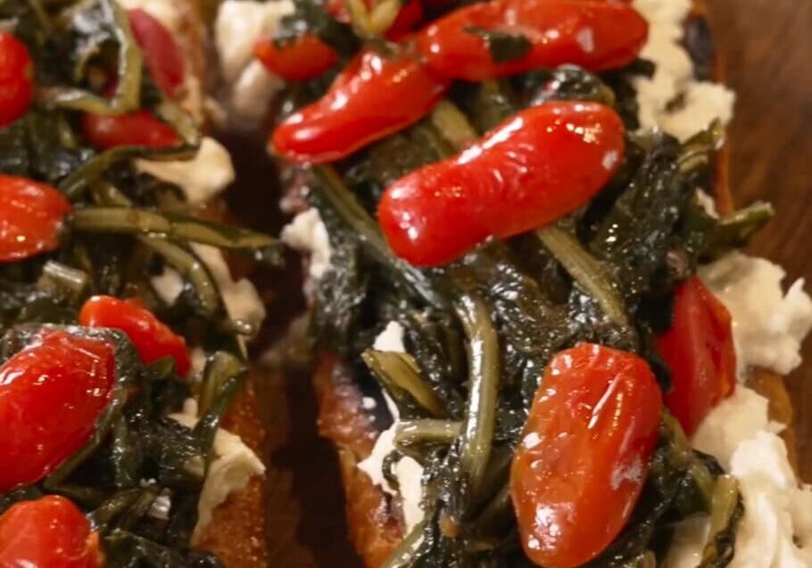 Two slices of toast topped with cream cheese, sautéed greens, and cherry tomatoes.