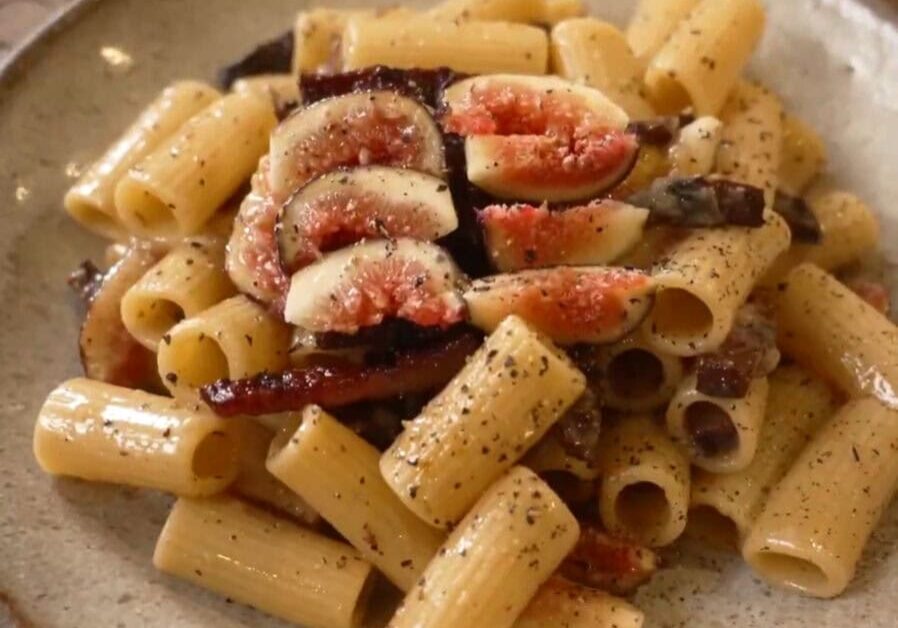 A plate of rigatoni pasta topped with sliced figs and red onion, seasoned with black pepper.