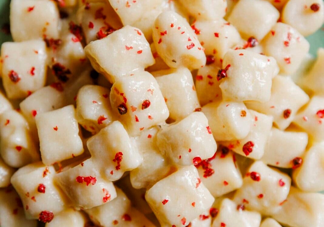 A plate of creamy gnocchi sprinkled with red pepper flakes, served on a green dish.