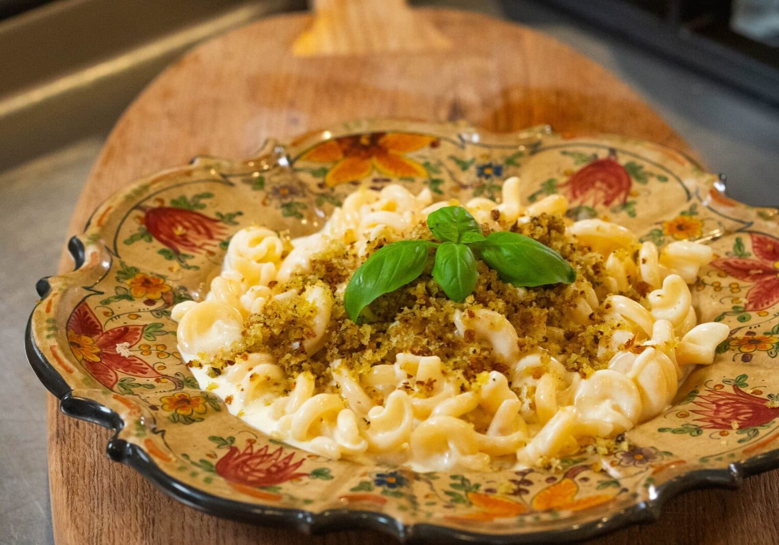A decorative plate of creamy pasta topped with breadcrumbs and garnished with fresh basil, placed on a wooden board.
