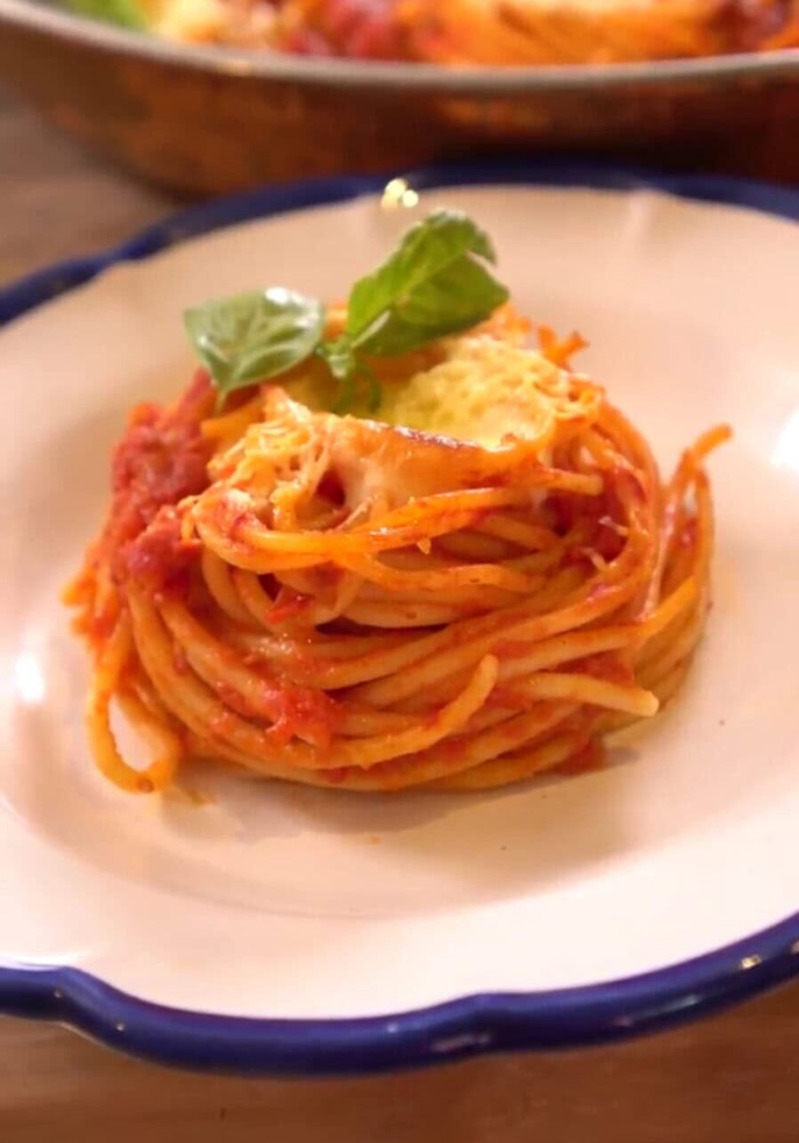 A plate of spaghetti with tomato sauce, garnished with basil leaves and a slice of cheese, served on a white dish with a blue rim.