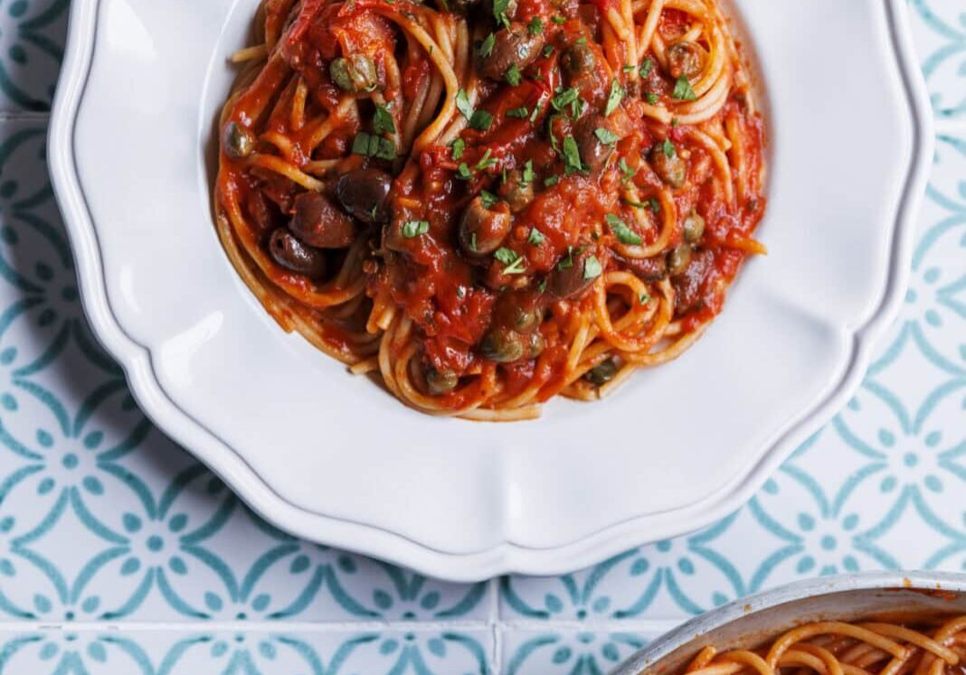 Plate of spaghetti with tomato sauce and herbs on a patterned blue and white tile surface.