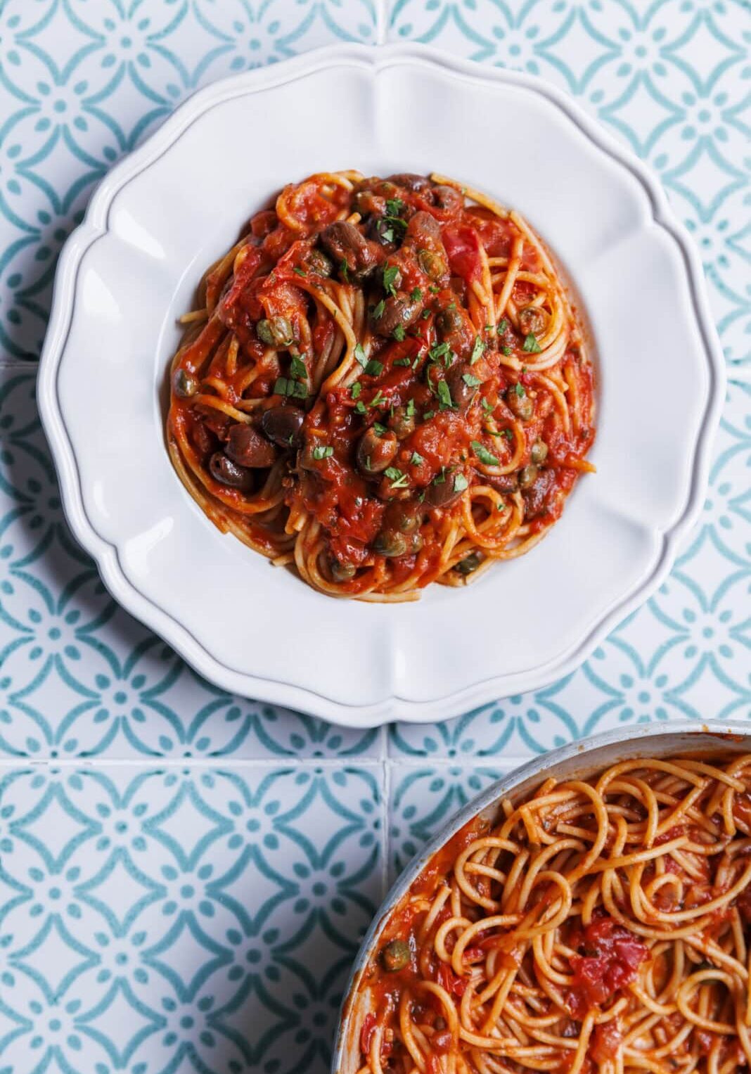 Plate of spaghetti with tomato sauce and herbs on a patterned blue and white tile surface.