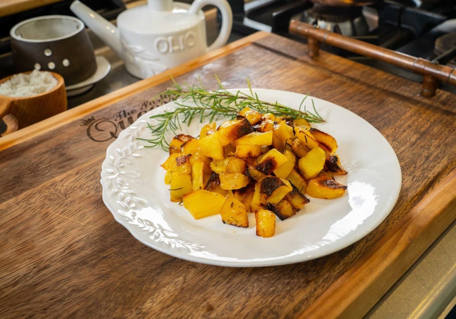 A plate of roasted yellow squash and zucchini garnished with rosemary on a wooden board in a kitchen setting.