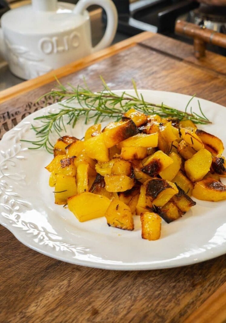 A plate of roasted yellow squash and zucchini garnished with rosemary on a wooden board in a kitchen setting.