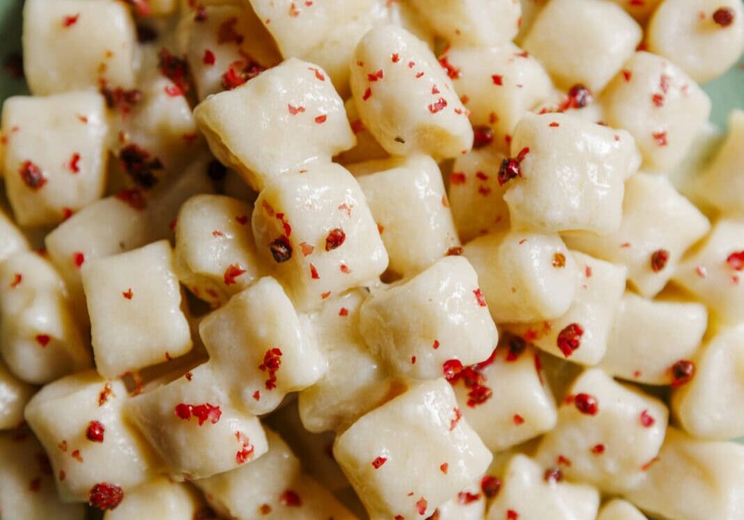 A plate of gnocchi in a creamy sauce, topped with a sprinkling of crushed pink peppercorns, served on a green ceramic dish.