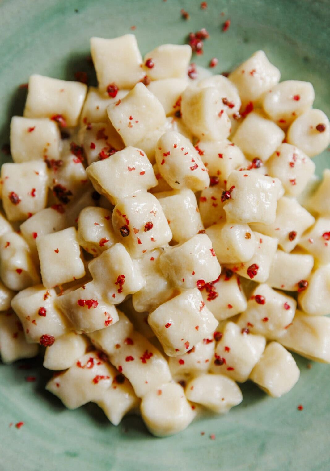 A plate of gnocchi in a creamy sauce, topped with a sprinkling of crushed pink peppercorns, served on a green ceramic dish.