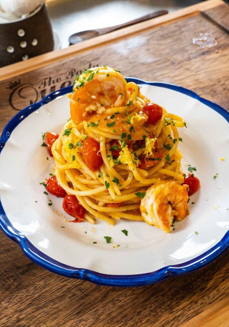 Plate of spaghetti topped with shrimp, cherry tomatoes, and parsley on a wooden board.