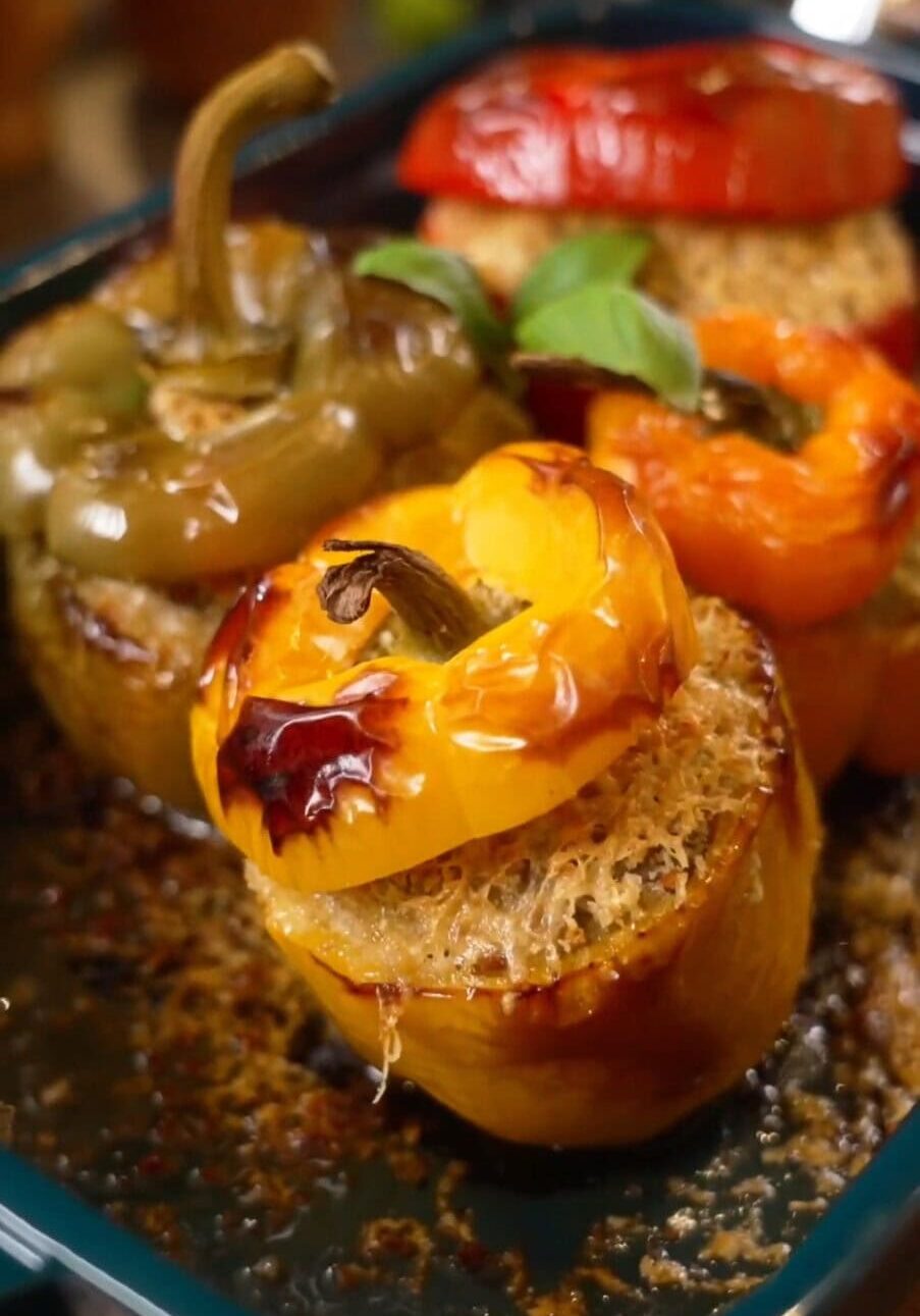 Three stuffed bell peppers (yellow, green, red) in a baking dish, filled with quinoa and topped with their respective caps.