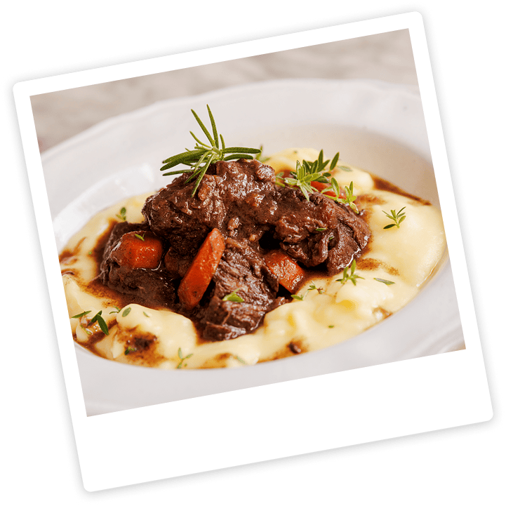 A plate of mashed potatoes topped with beef stew, carrots, and garnished with rosemary and thyme.