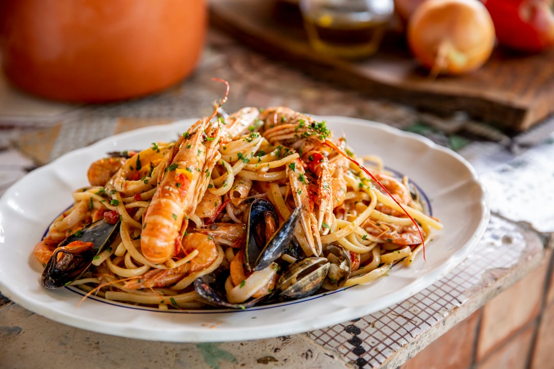 A plate of seafood pasta with shrimp, mussels, and clams in a tomato-based sauce, garnished with chopped herbs.