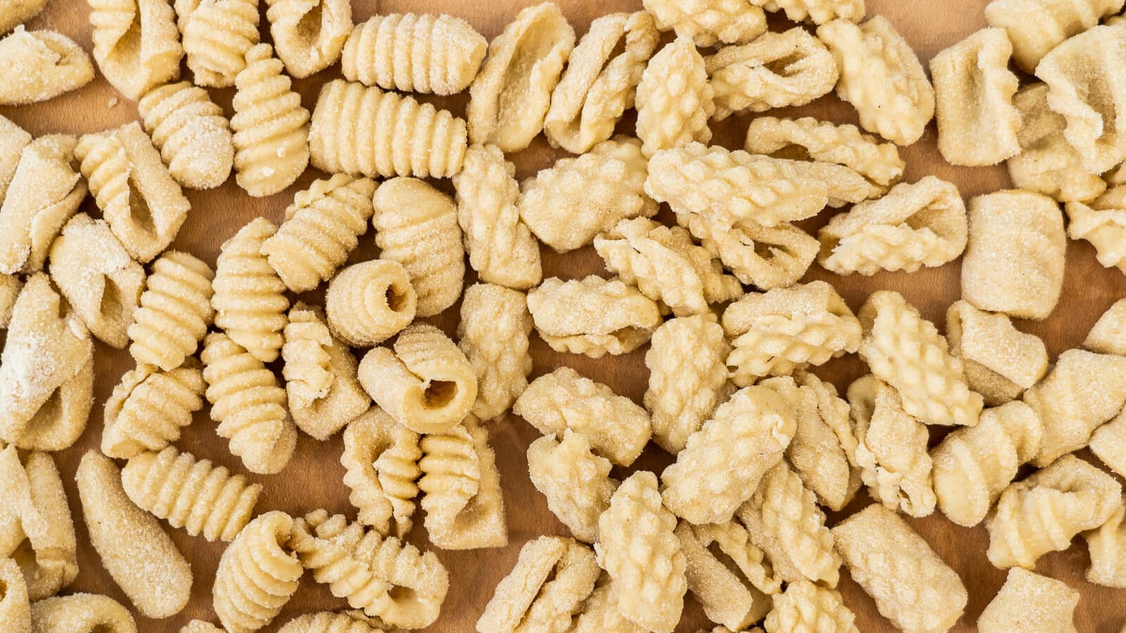 An assortment of uncooked, ridged pasta pieces with various shapes and textures spread out on a flat surface.